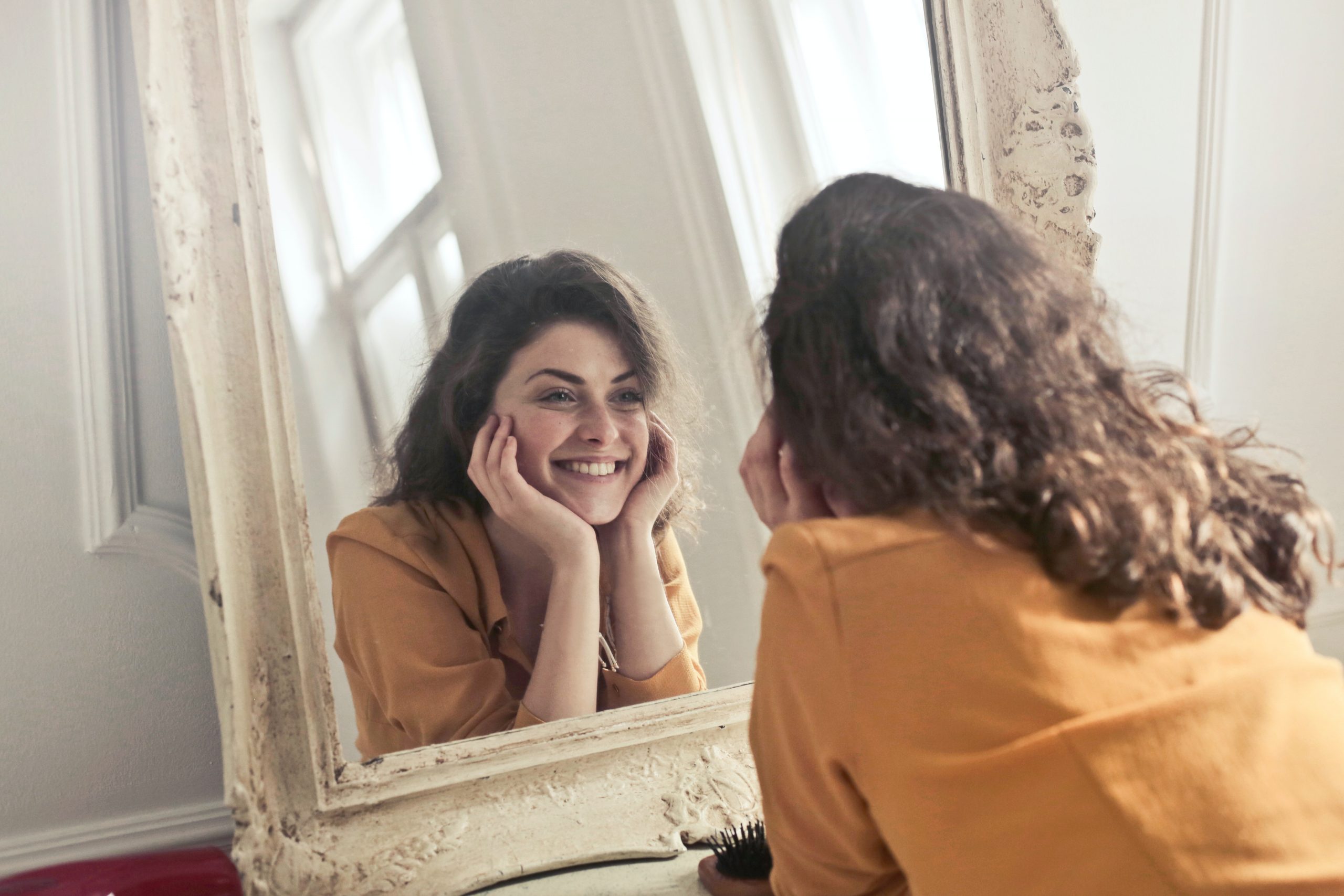 A woman smiling at her reflection in a naturally lit room